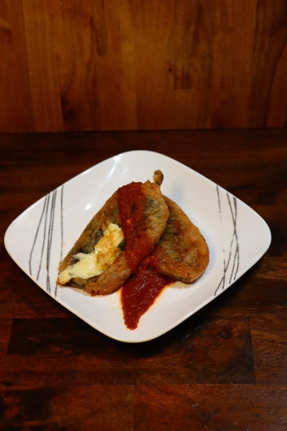 Chili rellenos on a white plate topped with red salsa