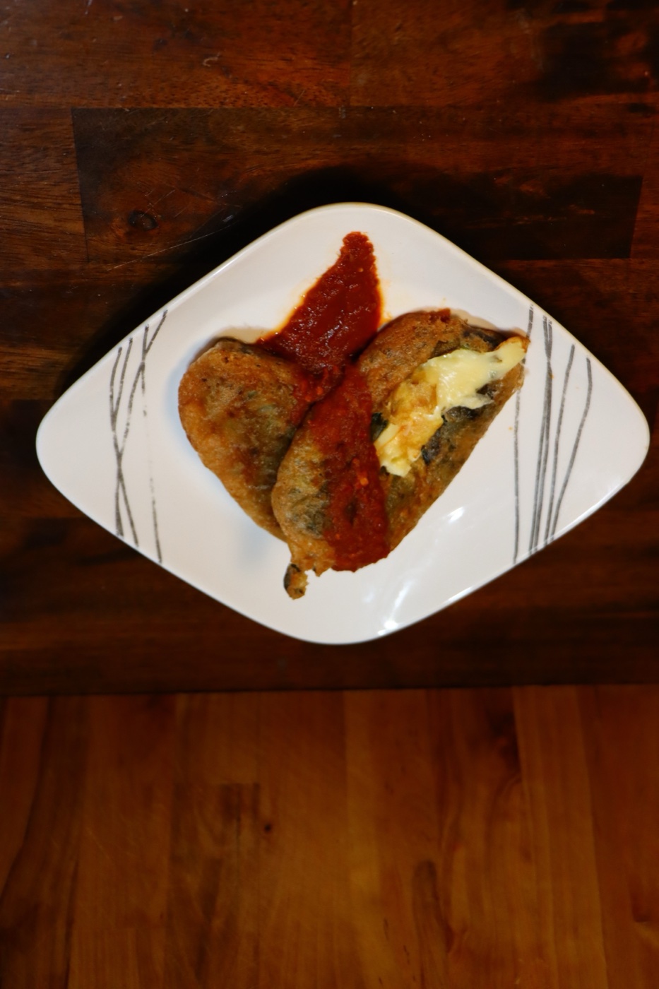 Chili rellenos on a white plate topped with red salsa